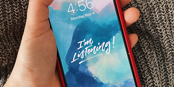 aerial view of hand holding smartphone with background wallpaper that says 'I'm Listening!'